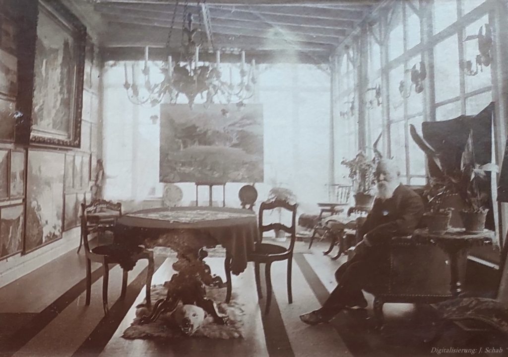 Foto von Ernst Seyffardt in der lichtdurchfluteten Wohnstube, im Hintergrund ein großformatiges Ölgemälde